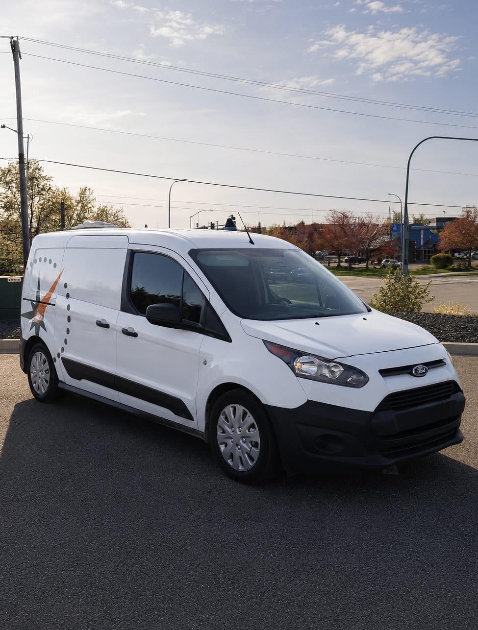 A white Ford Transit Connect cargo van with a partial orange and gray star decal on the side panel is parked in a parking lot under a clear sky.