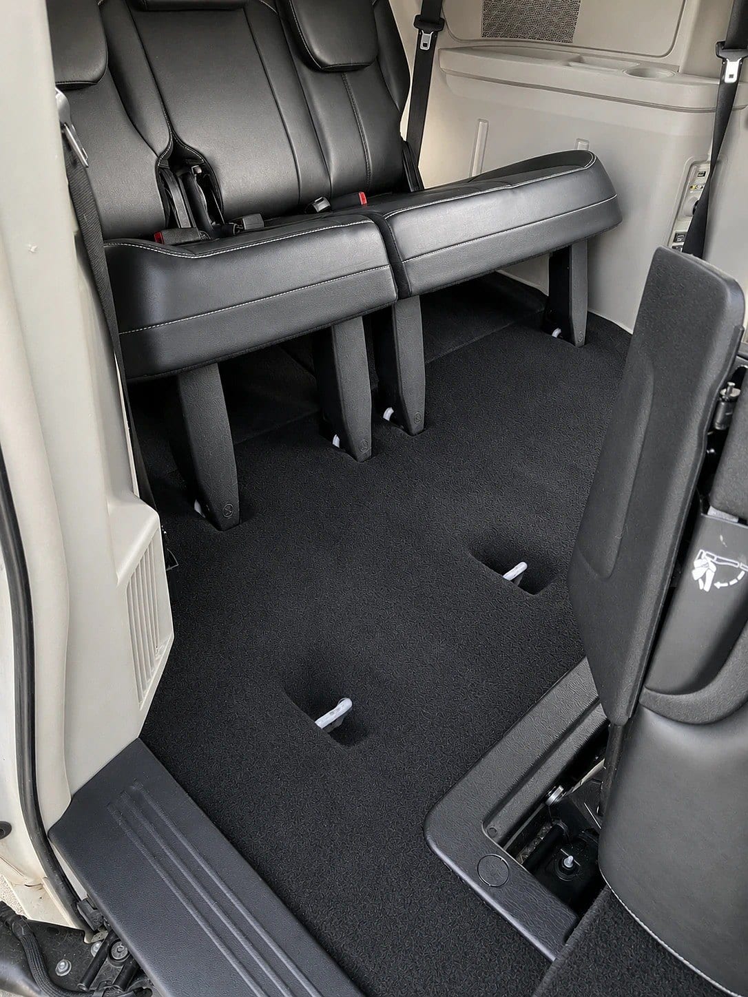 Interior of a minivan showing the rear cargo area with folded-down third-row seats and clean black carpet, viewed from the open side door.