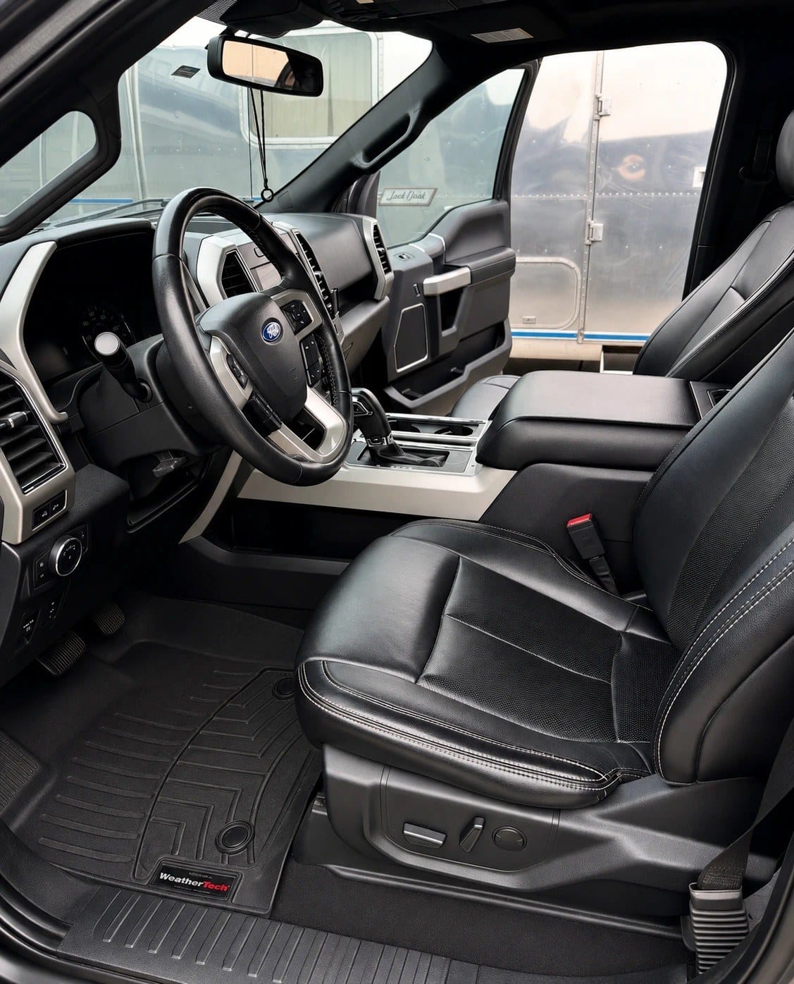 Clean black leather Ford pickup truck interior showing the driver’s seat, steering wheel with Ford badge, dashboard, and spotless floor mats, after detailing.
