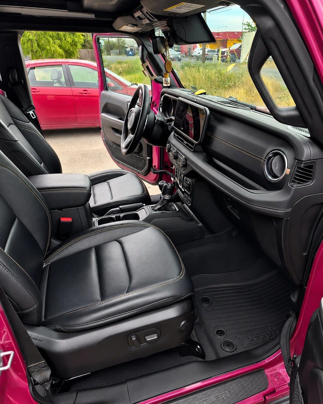 Clean black leather interior of a pink Jeep Wrangler showing the dashboard, steering wheel, center console, seats, and a clean rubber floor mat with a visible Jeep logo, after detailing.